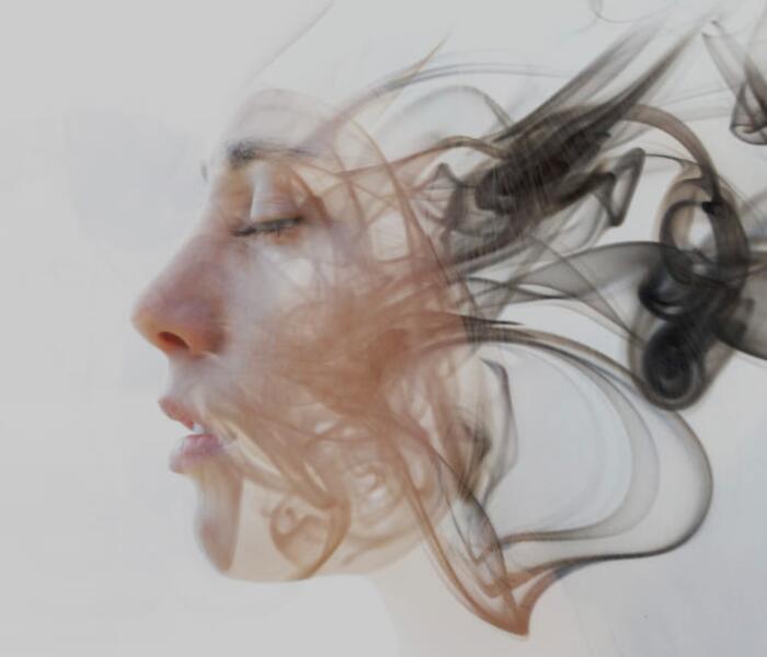 Double-exposure profile of a woman dissolving into drifting smoke